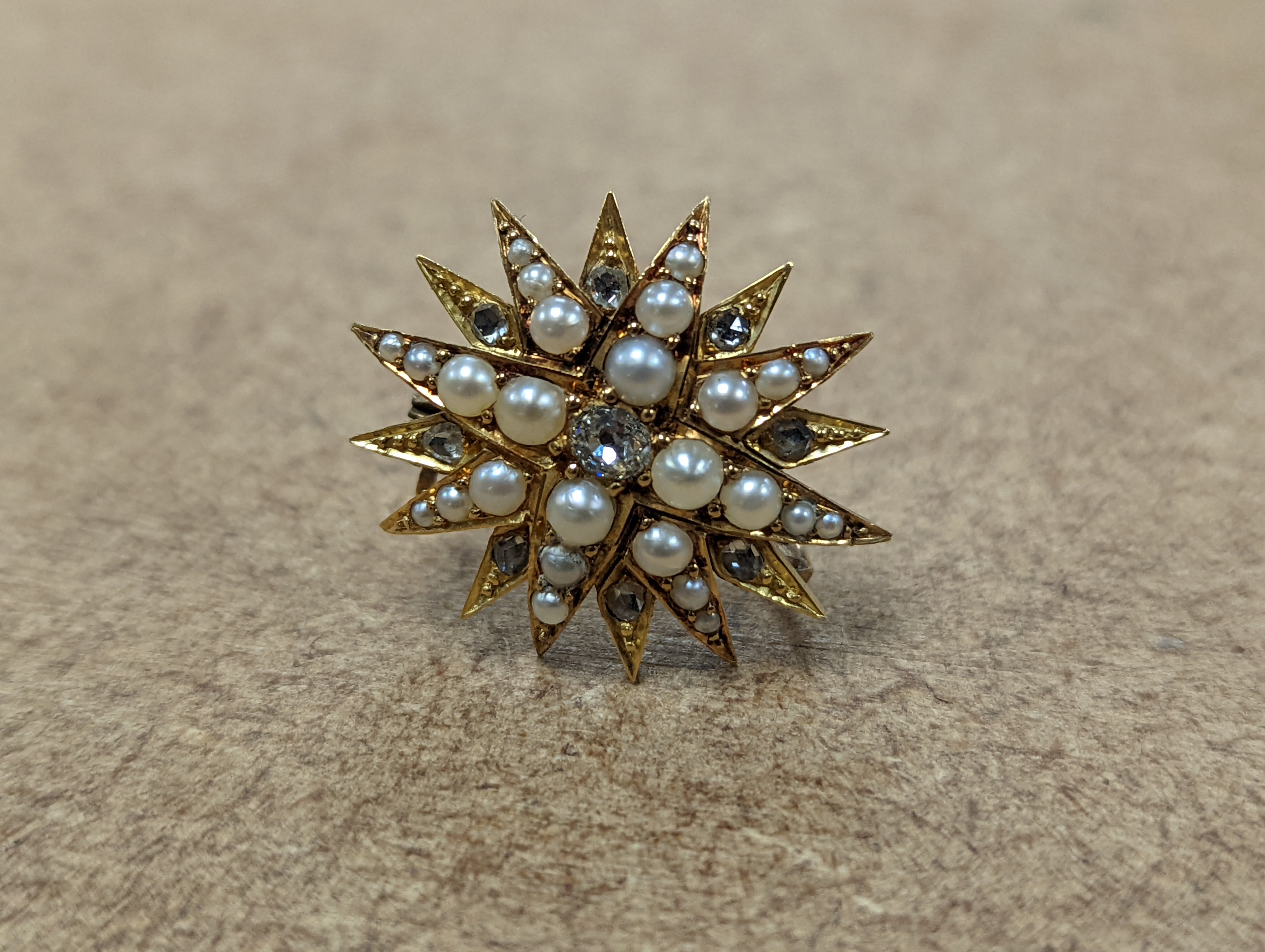 An Edwardian yellow metal, graduated split pearl and single stone diamond set starburst brooch(adapted?), 24mm, gross weight 6.5 grams.